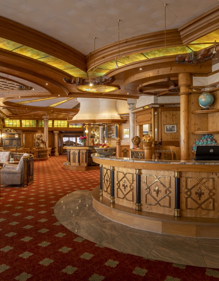 Luxuriöse Hotel-Lobby mit Holzregalen und einer eleganten Rezeption, dekoriert mit antiken Möbeln und einem künstlerischen Glaskunstwerk an der Decke.