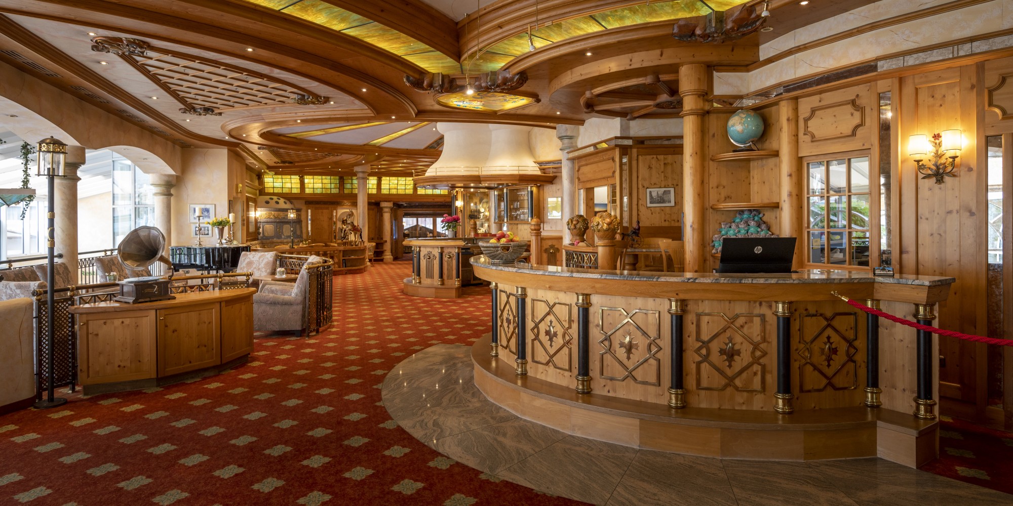 Luxuriöse Hotel-Lobby mit Holzregalen und einer eleganten Rezeption, dekoriert mit antiken Möbeln und einem künstlerischen Glaskunstwerk an der Decke.